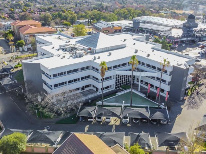 Aerial view of a multi-story commercial office building featuring a central skylight, extensive covered parking, and landscaped grounds in a suburban business district.