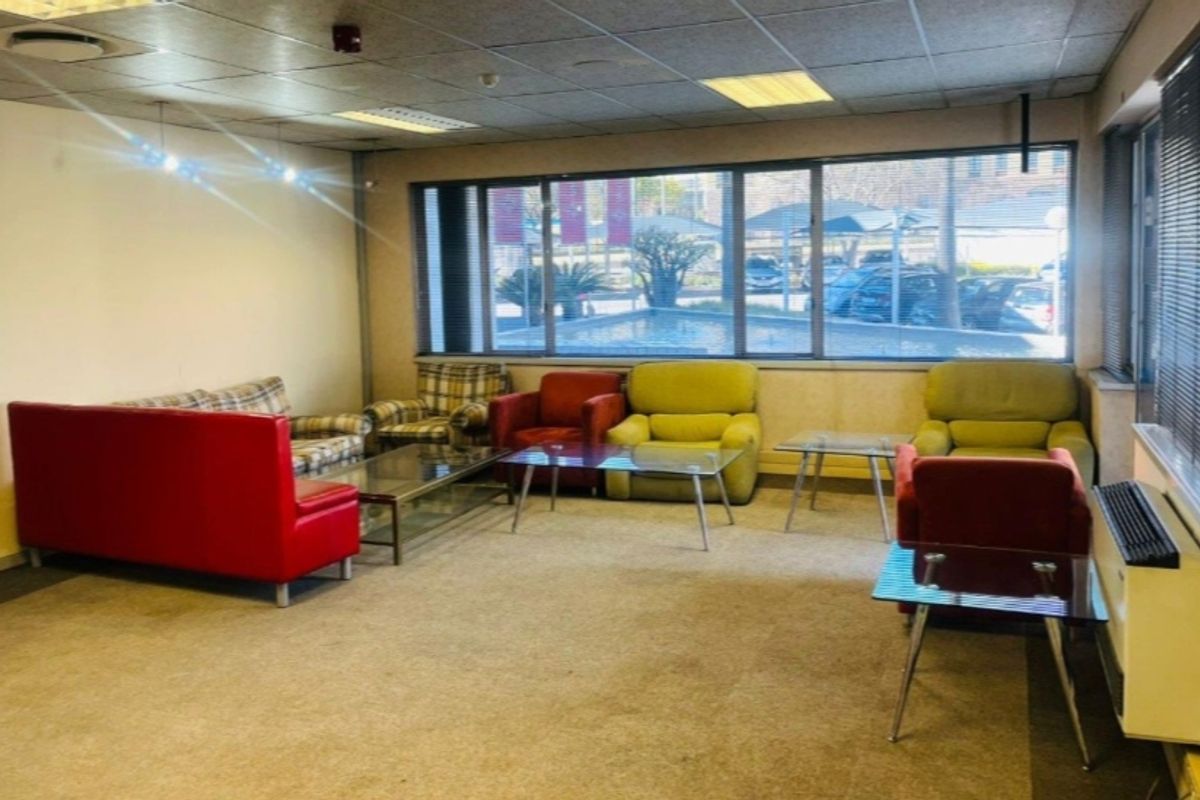 A commercial waiting area or lounge featuring large windows, suspended ceiling tiles, and carpeted flooring, offering a functional space for clients or staff.