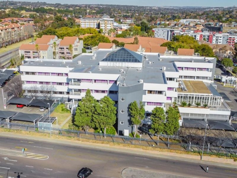 Aerial view of a multi-story commercial office building featuring a central pyramid skylight, extensive covered parking, and secure perimeter fencing.