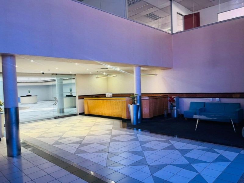 Spacious commercial building entrance lobby featuring a built-in reception desk, tiled flooring, and glass partitions leading to an open-plan office area.