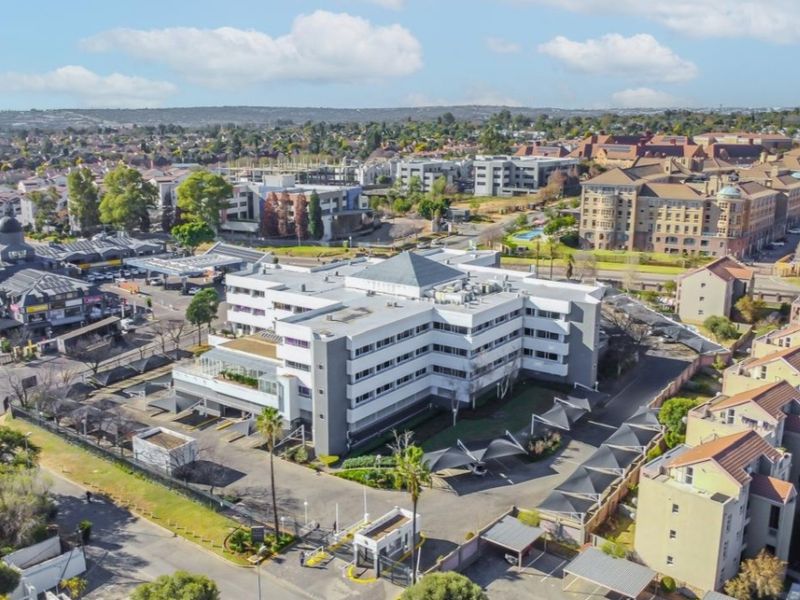 Aerial view of a multi-story commercial office building featuring extensive parking facilities, security access control, and landscaped surroundings in a suburban business node.