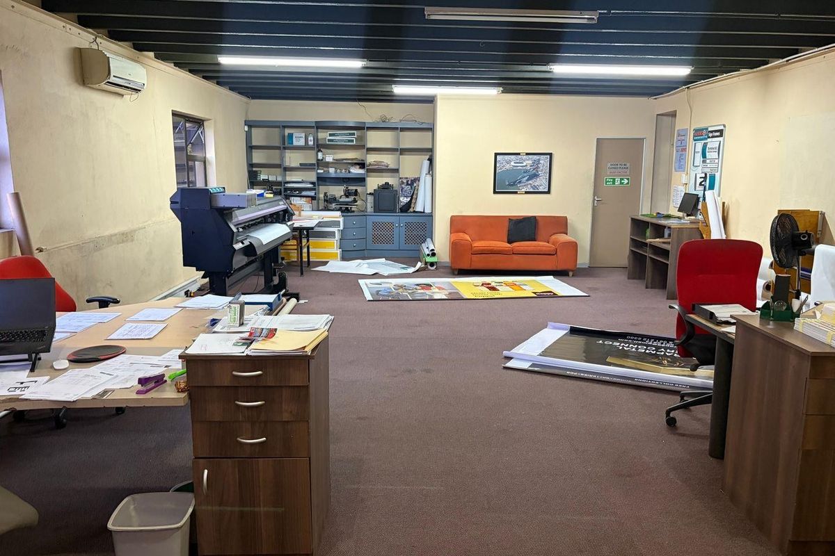 A spacious office area featuring exposed ceiling beams, built-in shelving, and a split-system air conditioner, currently utilized as a workspace.