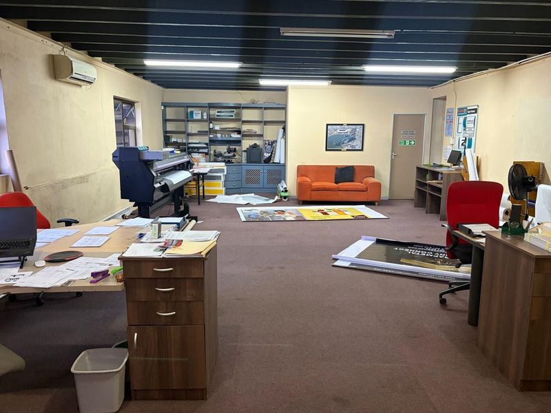 A spacious office area featuring exposed ceiling beams, built-in shelving, and a split-system air conditioner, currently utilized as a workspace.