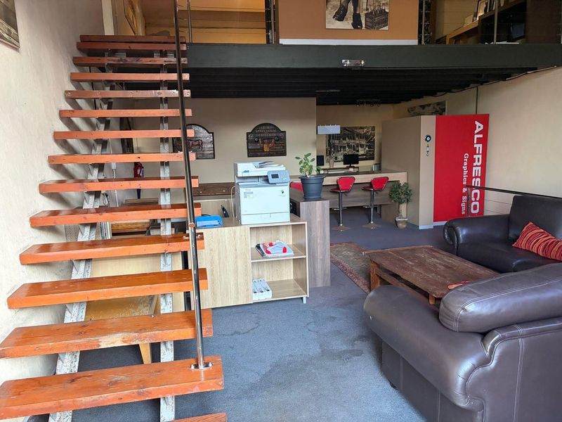 Open-plan commercial or residential space featuring a mezzanine level, an open staircase, and a built-in counter area with carpeted flooring.