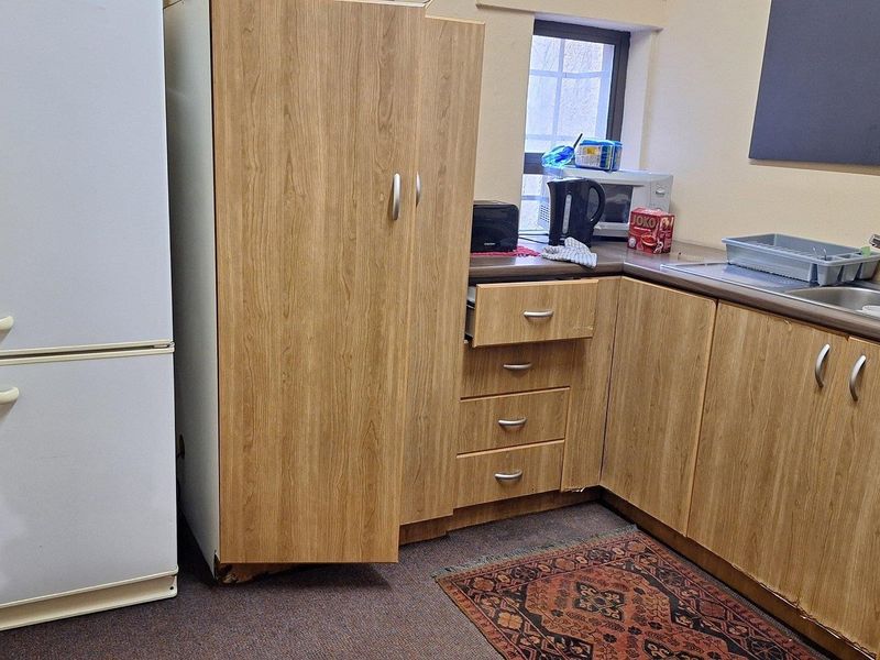 A compact kitchen area featuring wood-look laminate cabinetry, a stainless steel sink, and basic countertop space, currently showing signs of wear.