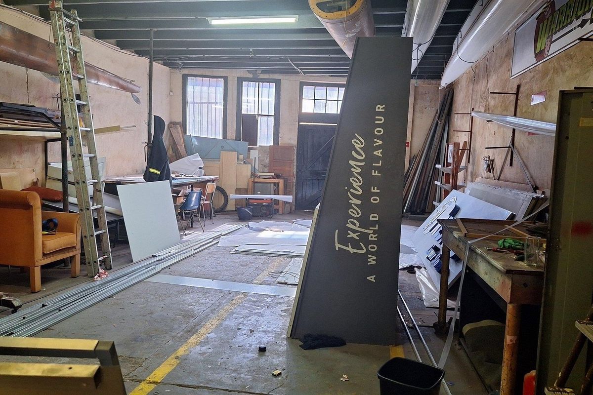 A large, industrial-style utility space featuring exposed ceiling beams, concrete flooring, and large windows, currently used for storage.