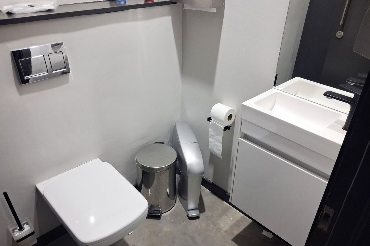 A modern commercial bathroom featuring a wall-mounted toilet with a concealed cistern, a sleek vanity cabinet with an integrated sink, and a wall-mounted mirror.