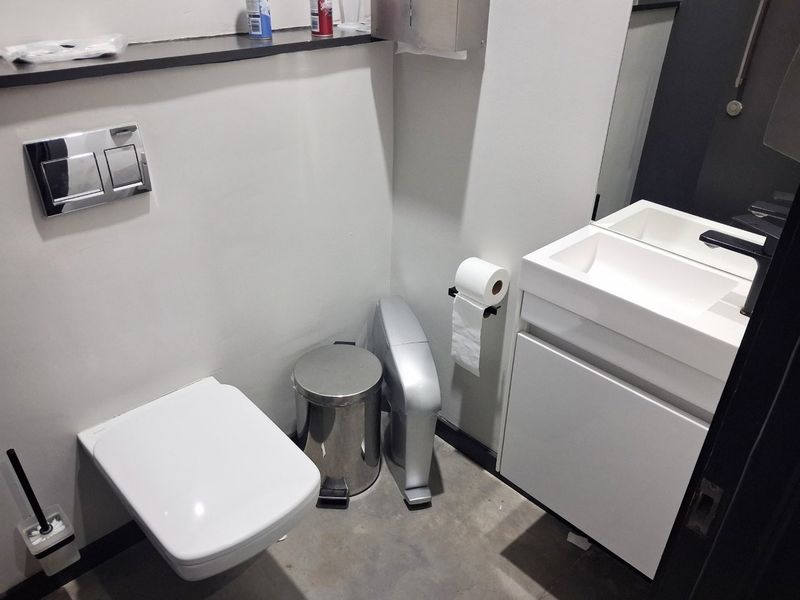 A modern commercial bathroom featuring a wall-mounted toilet with a concealed cistern, a sleek vanity cabinet with an integrated sink, and a wall-mounted mirror.