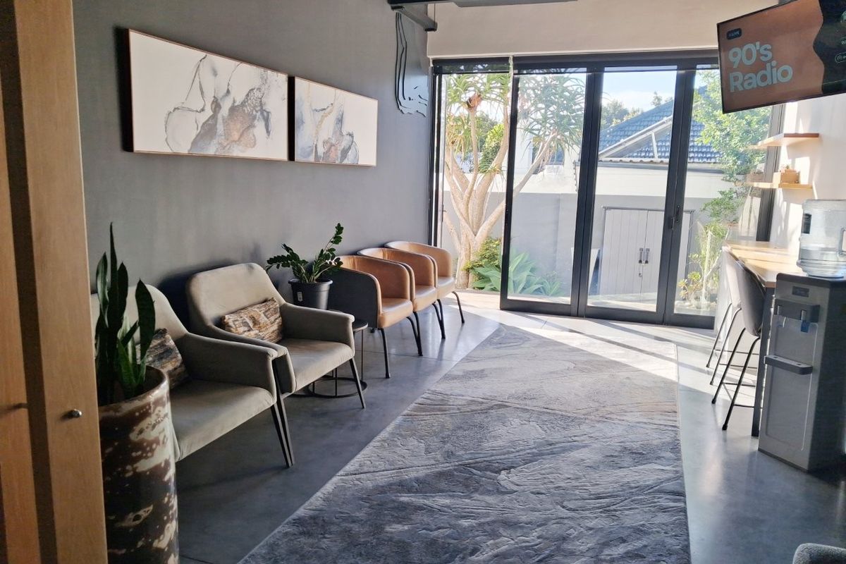 Modern commercial waiting area featuring polished concrete floors, exposed ceiling ducting, and large sliding glass doors providing natural light and garden access.