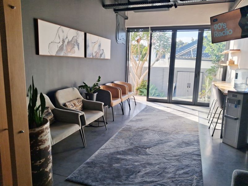 Modern commercial waiting area featuring polished concrete floors, exposed ceiling ducting, and large sliding glass doors providing natural light and garden access.