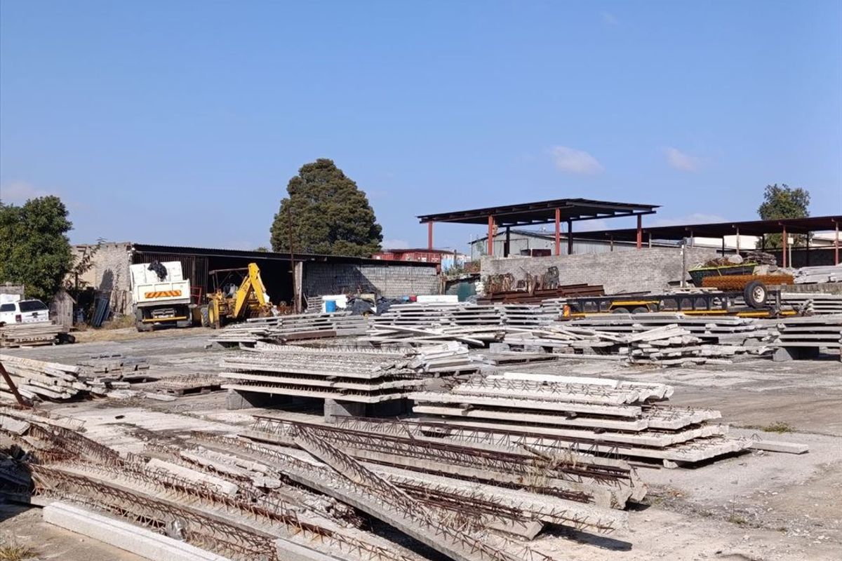 Industrial yard space featuring a concrete surface, perimeter walling, and an open-sided storage shed structure.