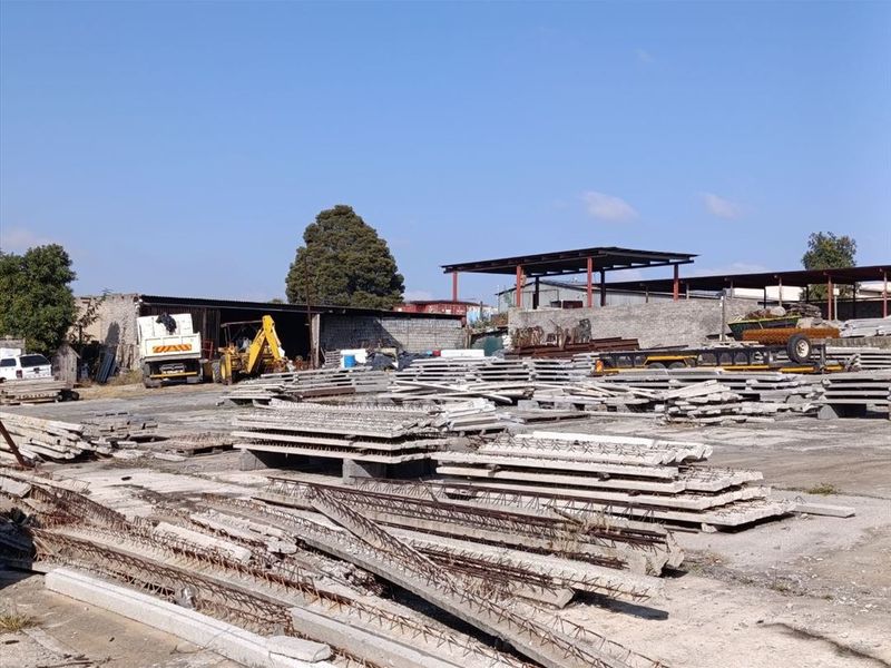 Industrial yard space featuring a concrete surface, perimeter walling, and an open-sided storage shed structure.