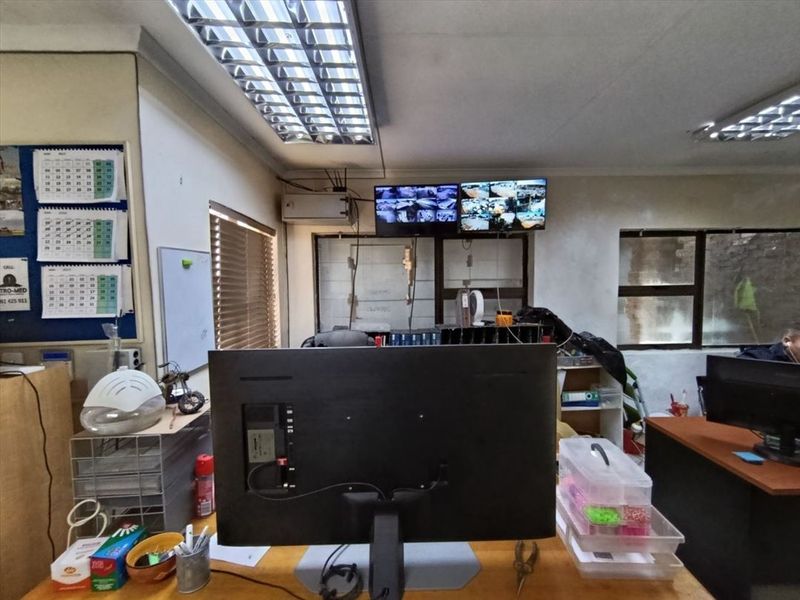Functional industrial office space featuring overhead fluorescent lighting, venetian blinds, and a wall-mounted CCTV monitoring system.