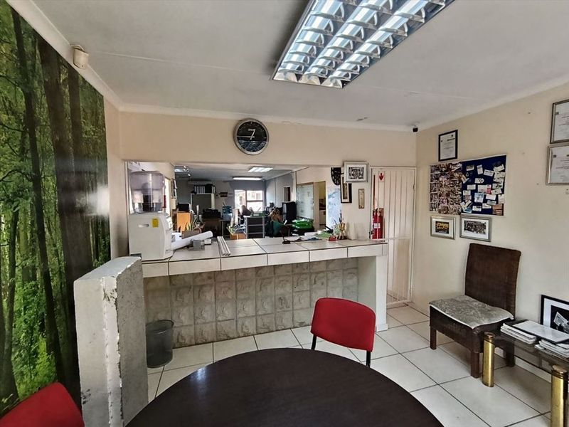 Functional office reception area featuring a service counter, tiled flooring, and overhead fluorescent lighting, suitable for administrative or industrial business operations.