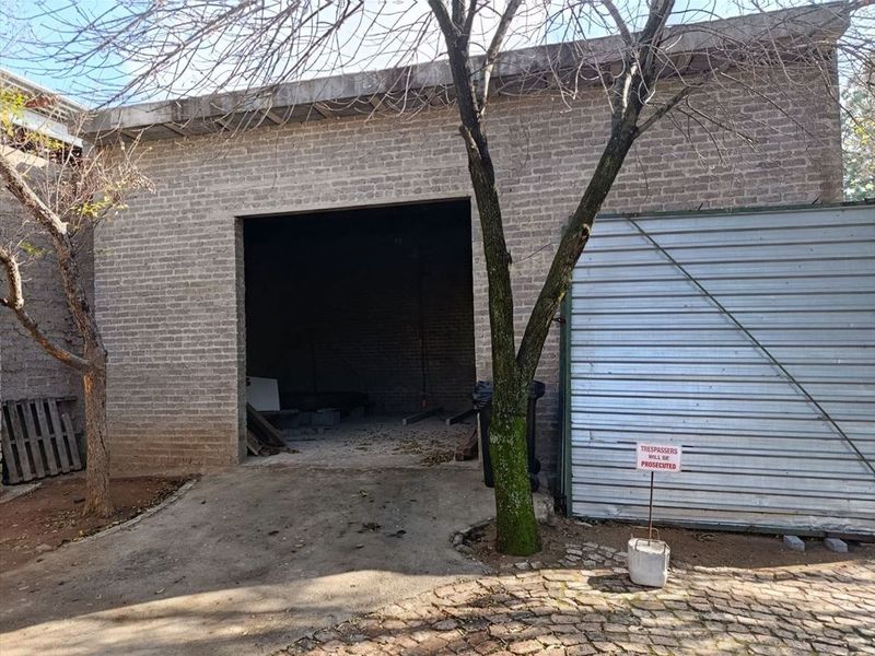 Industrial property exterior featuring a brick facade, a large open entrance, and a corrugated metal roller door with a paved driveway area.