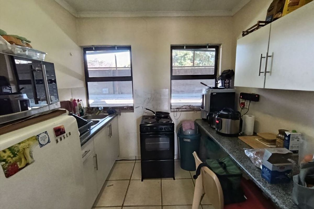 A compact industrial kitchen featuring tiled flooring, laminate countertops, built-in cabinetry, and a freestanding stove, requiring cosmetic updates to improve its overall condition.