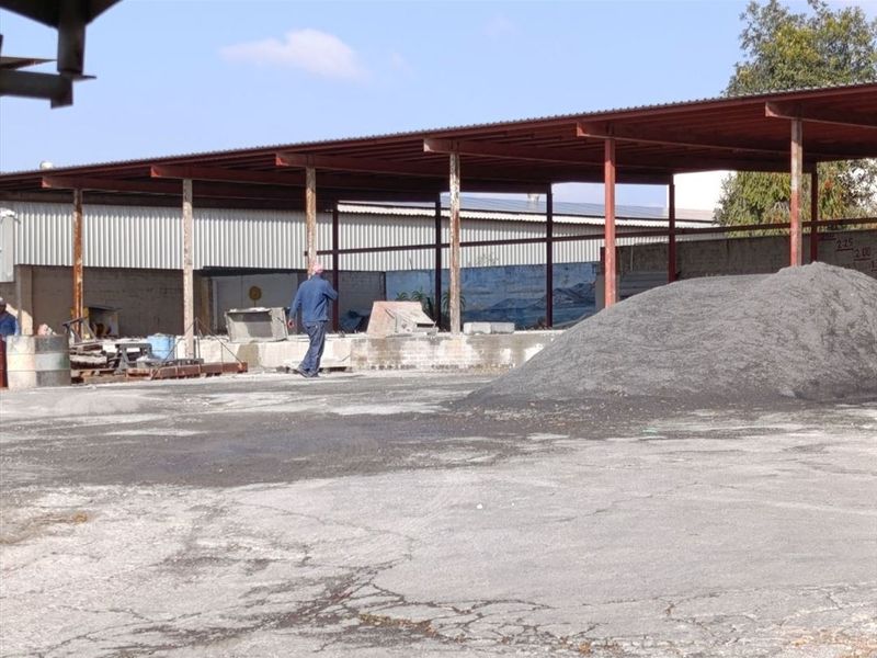 Industrial yard area featuring a large covered steel structure, concrete paving, and perimeter walling, suitable for storage or operational use.
