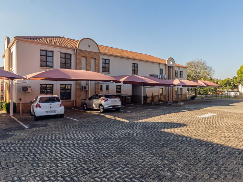 Exterior view of a two-story office building featuring a paved parking area with multiple shade cloth carports and external air conditioning units.