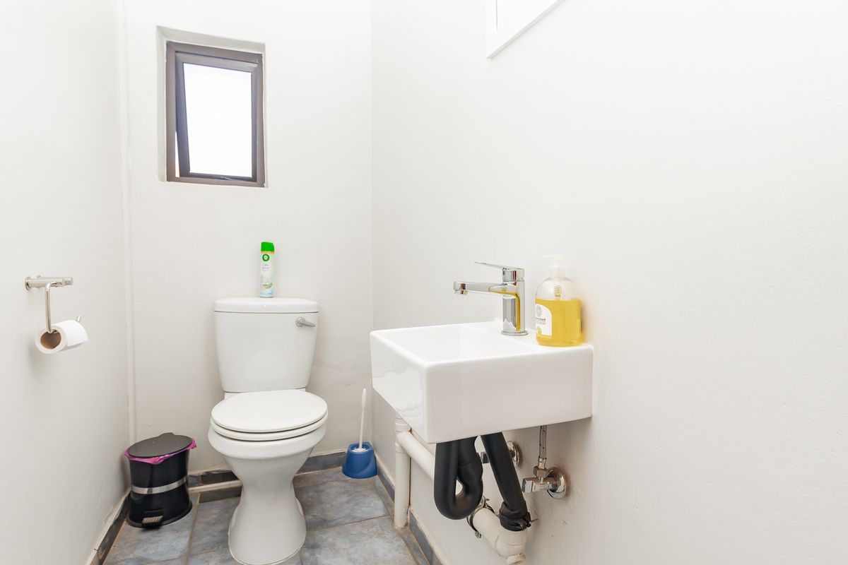 A compact office restroom featuring a white toilet, wall-mounted basin with chrome mixer tap, and tiled flooring.