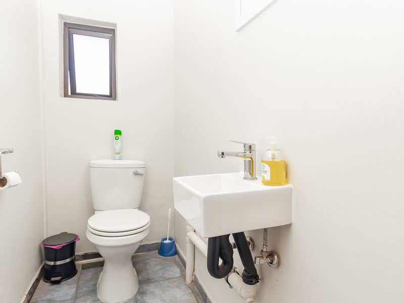 A compact office restroom featuring a white toilet, wall-mounted basin with chrome mixer tap, and tiled flooring.