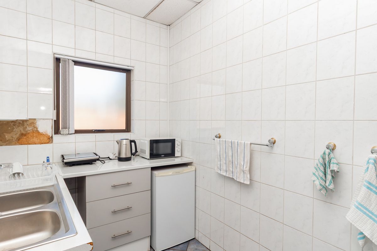 A compact kitchenette featuring tiled walls, a double bowl stainless steel sink, and built-in cabinetry, requiring minor repairs to wall finishes and countertops.