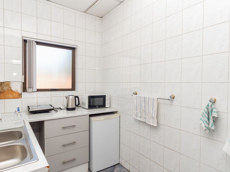 A compact kitchenette featuring tiled walls, a double bowl stainless steel sink, and built-in cabinetry, requiring minor repairs to wall finishes and countertops.