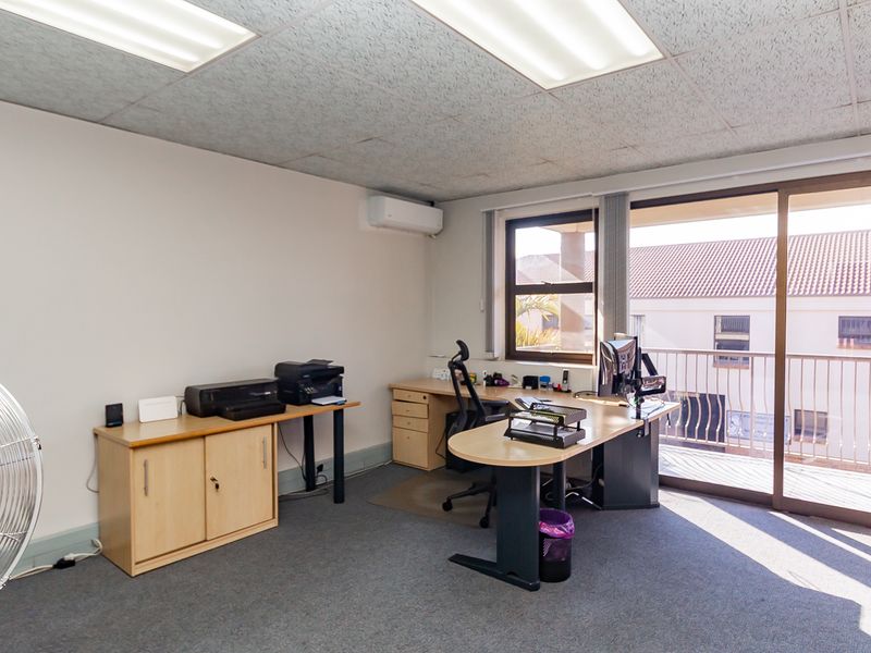 A functional office space featuring carpeted flooring, built-in air conditioning, and a sliding glass door providing access to a private balcony.