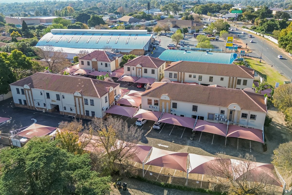 Aerial view of a multi-building office complex featuring tiled roofs, paved parking areas with shade cloth carports, and established landscaping.