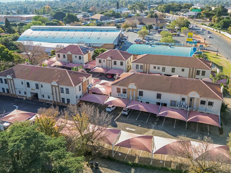 Aerial view of a multi-building office complex featuring tiled roofs, paved parking areas with shade cloth carports, and established landscaping.