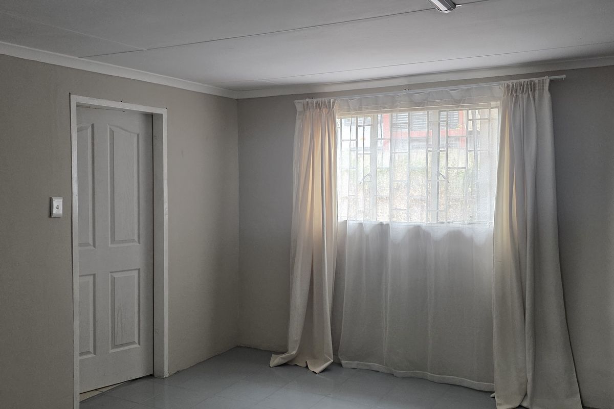 A clean, empty office space featuring neutral wall tones, tiled flooring, and a window fitted with security bars.