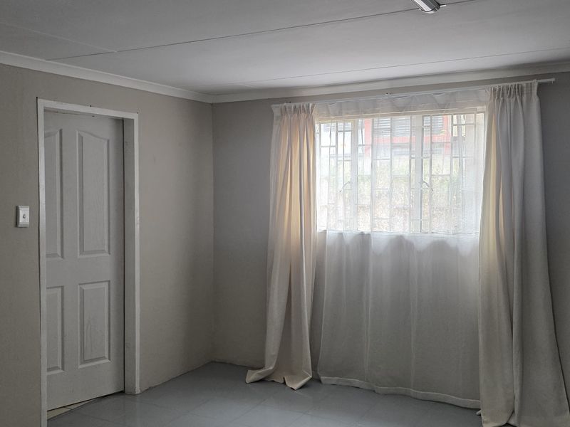 A clean, empty office space featuring neutral wall tones, tiled flooring, and a window fitted with security bars.