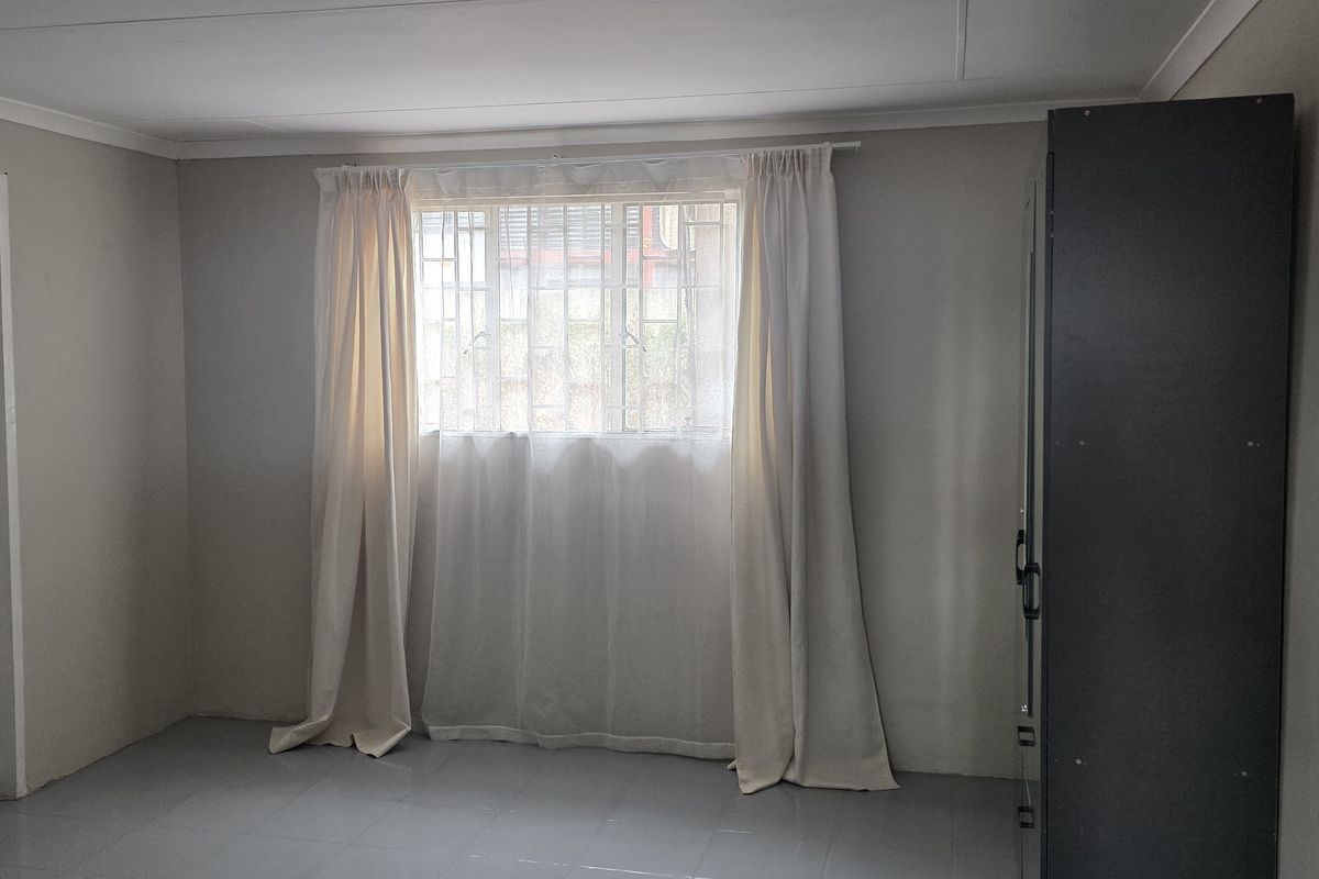 A functional office space featuring tiled flooring and a window fitted with security bars.