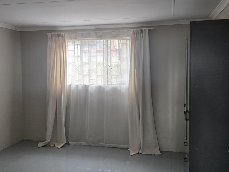 A functional office space featuring tiled flooring and a window fitted with security bars.