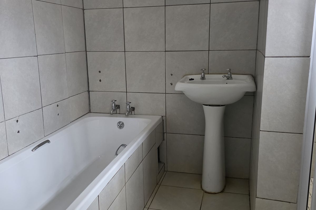 A functional bathroom featuring a built-in bathtub, pedestal basin, and separate shower enclosure with neutral ceramic tiling throughout.