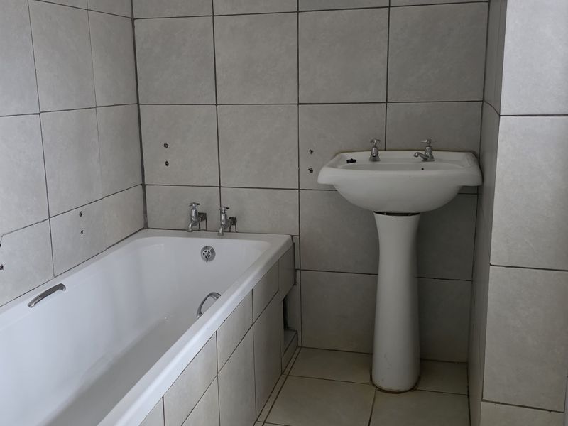 A functional bathroom featuring a built-in bathtub, pedestal basin, and separate shower enclosure with neutral ceramic tiling throughout.