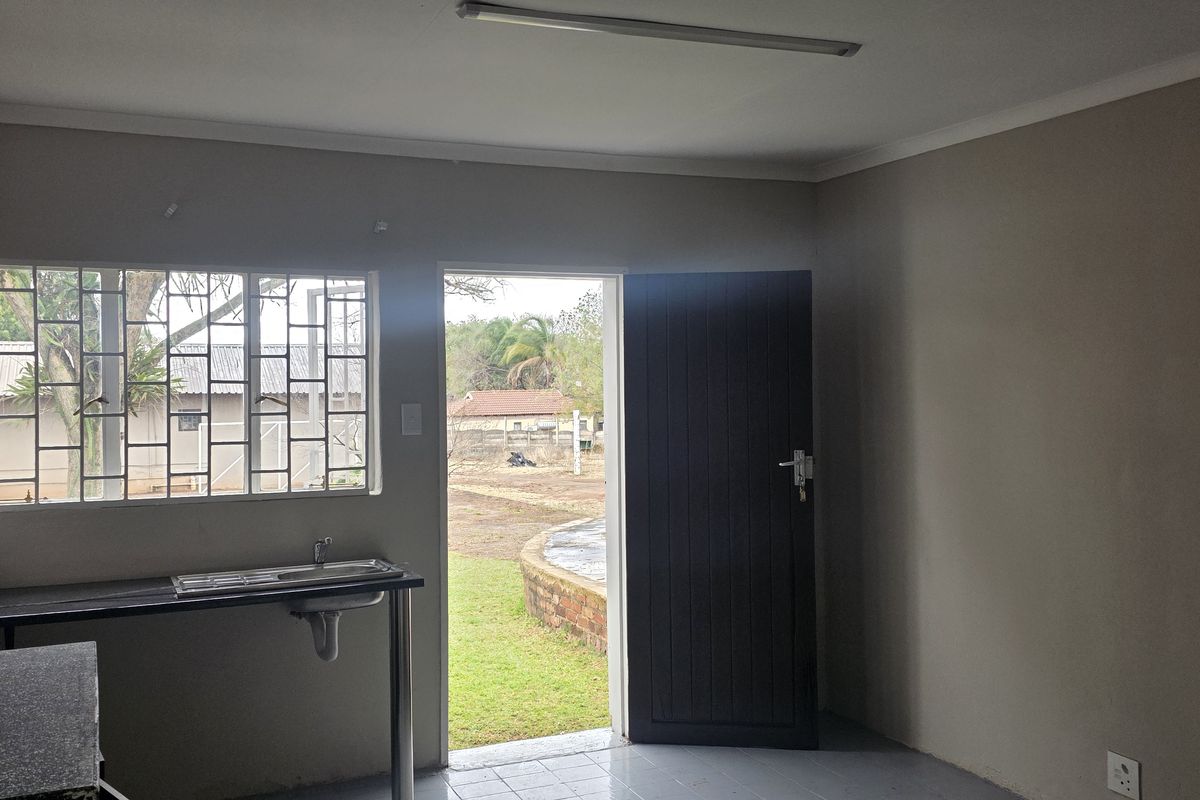 A compact, empty office kitchenette featuring a stainless steel sink, tiled flooring, and direct access to the exterior through a single door.