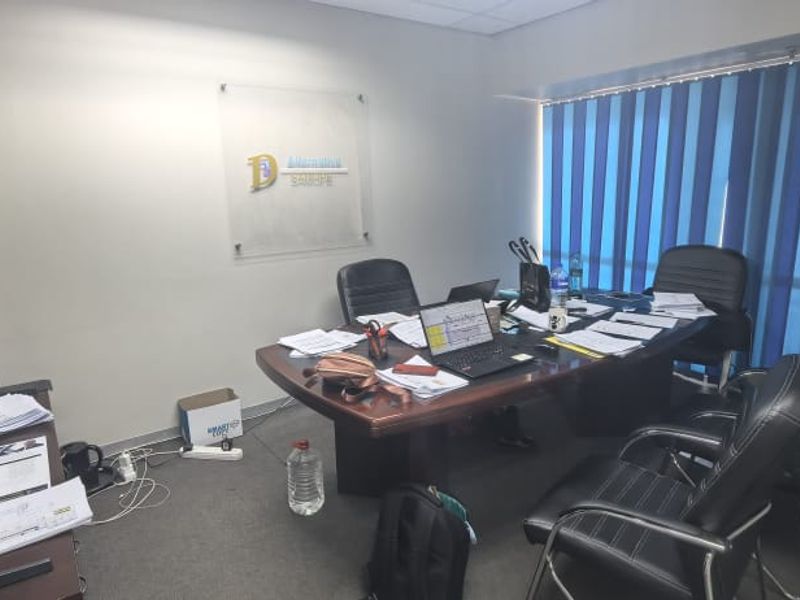 A functional office space featuring carpeted flooring, a suspended ceiling, and vertical window blinds, suitable for professional use.