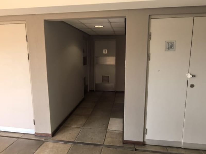 A functional office hallway featuring tiled flooring, recessed ceiling lights, and multiple access doors to utility or service areas.