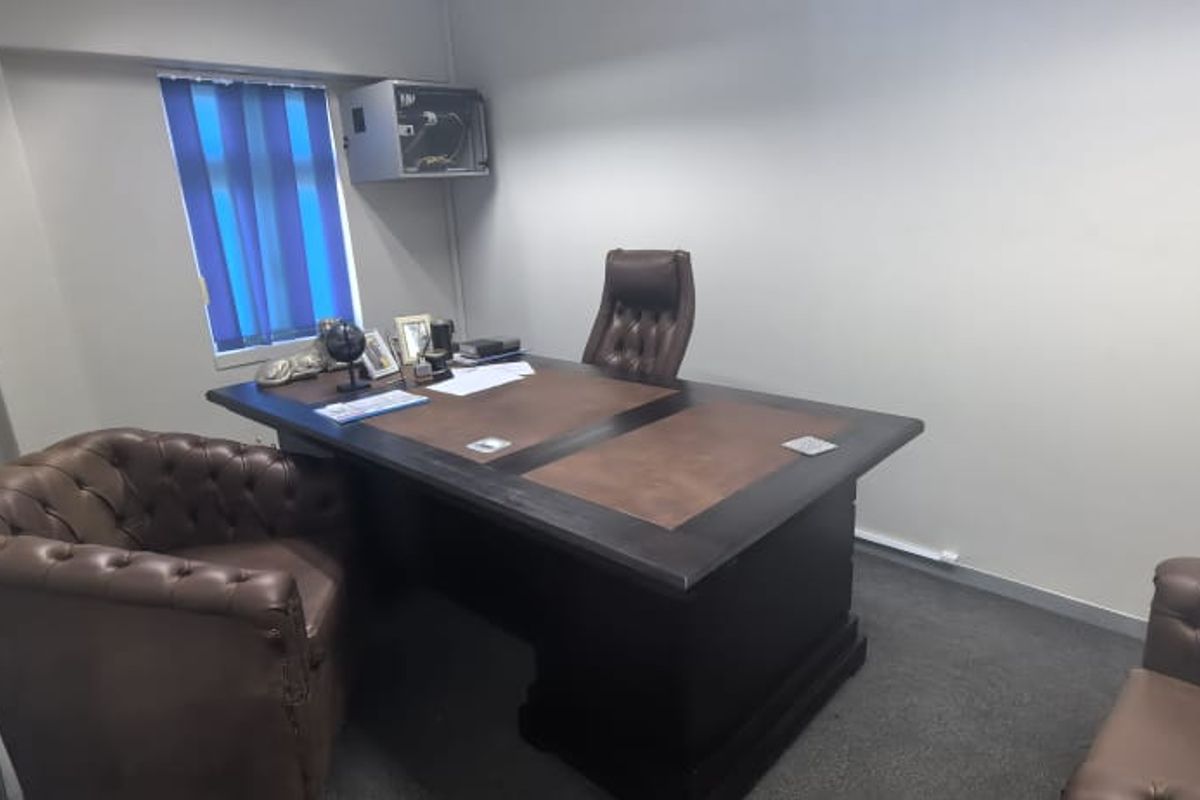 A functional office space featuring carpeted flooring, vertical window blinds, and a wall-mounted electrical distribution box.