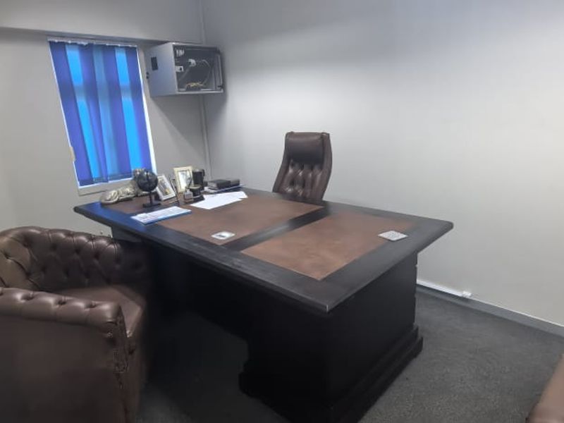 A functional office space featuring carpeted flooring, vertical window blinds, and a wall-mounted electrical distribution box.