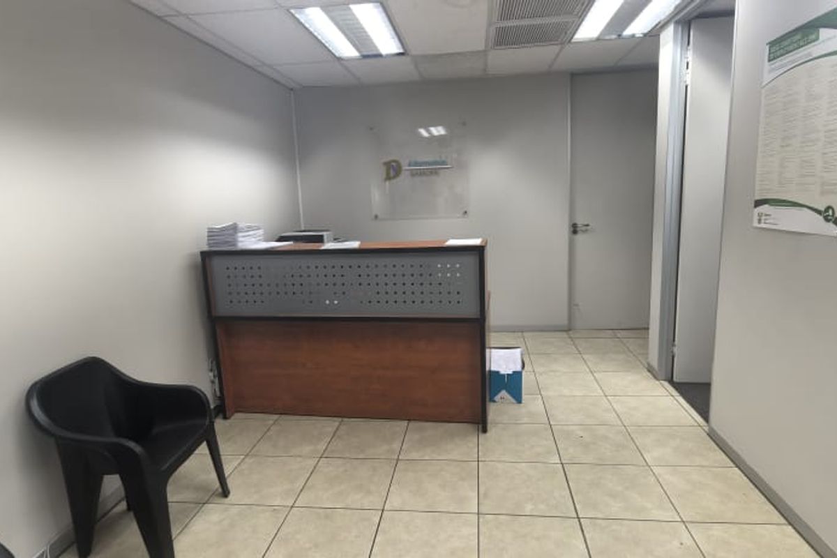 A functional office reception area featuring ceramic floor tiles, a built-in reception desk, and recessed ceiling lighting.