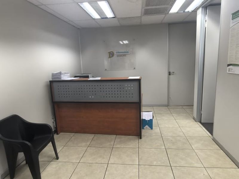 A functional office reception area featuring ceramic floor tiles, a built-in reception desk, and recessed ceiling lighting.