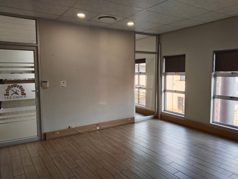 A bright, vacant office space featuring modern timber-look floor tiles, suspended ceilings with recessed lighting, and aluminium-framed glass partitions.