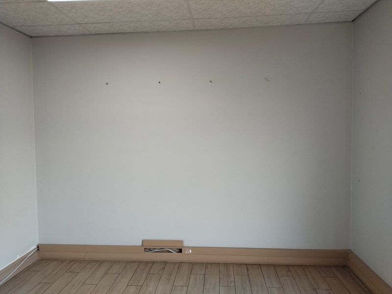 An empty office space featuring wood-look tile flooring, a suspended ceiling, and integrated skirting board trunking for electrical and data connectivity.