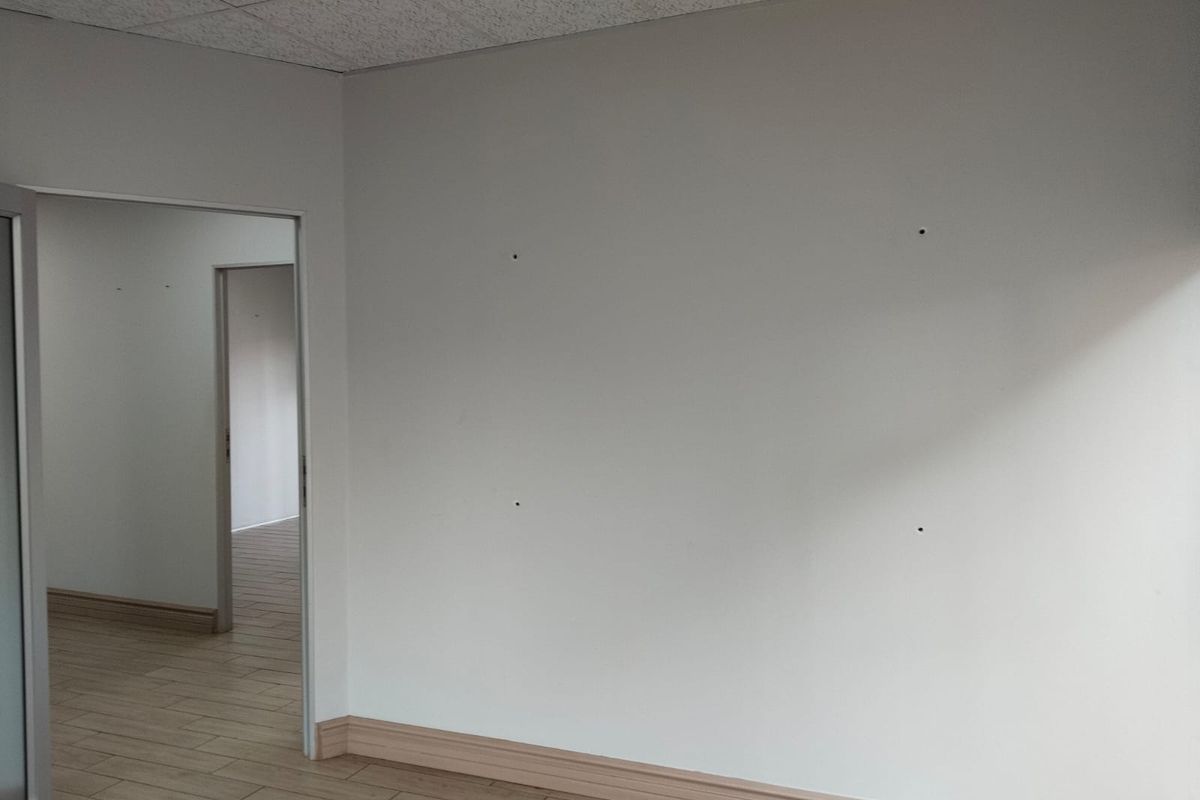 An empty office space featuring tiled flooring, a suspended ceiling, and neutral walls with minor surface imperfections.