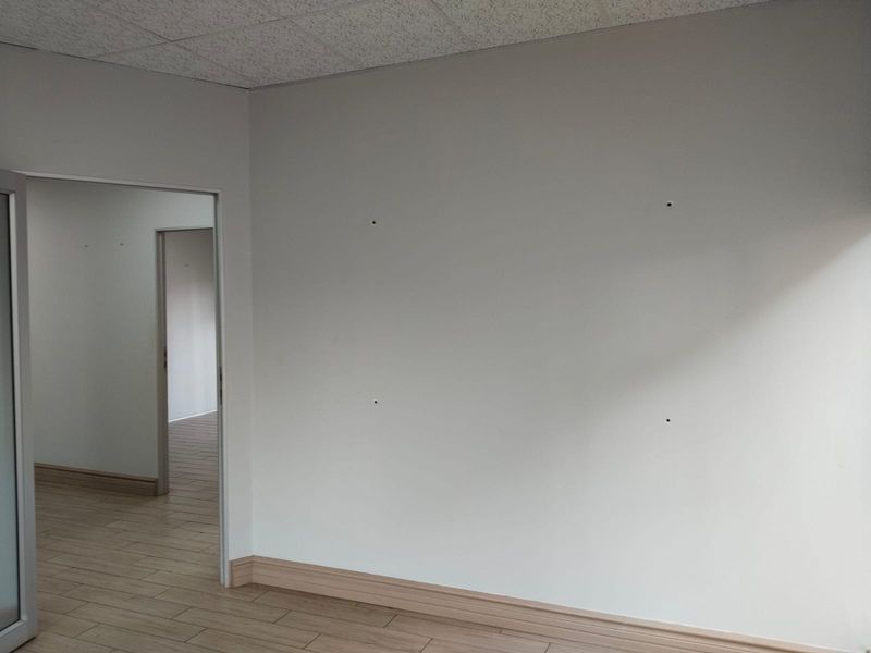 An empty office space featuring tiled flooring, a suspended ceiling, and neutral walls with minor surface imperfections.