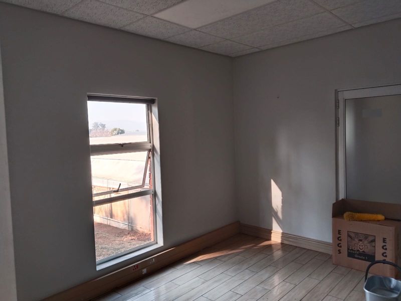 A bright, empty office space featuring tiled flooring, a suspended ceiling, and natural light from a large window.