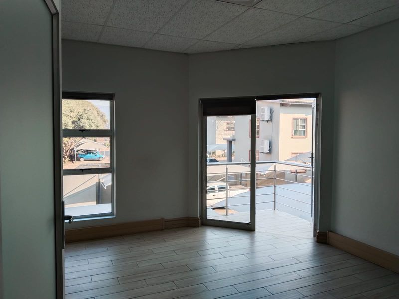 A bright, empty office space featuring tiled flooring, a suspended ceiling, and direct access to a private balcony through a sliding glass door.