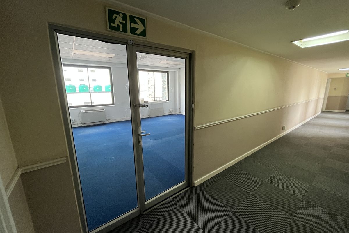 A view of an office hallway with carpeted flooring, chair rail detailing, and a glass-paneled door leading into an office suite.