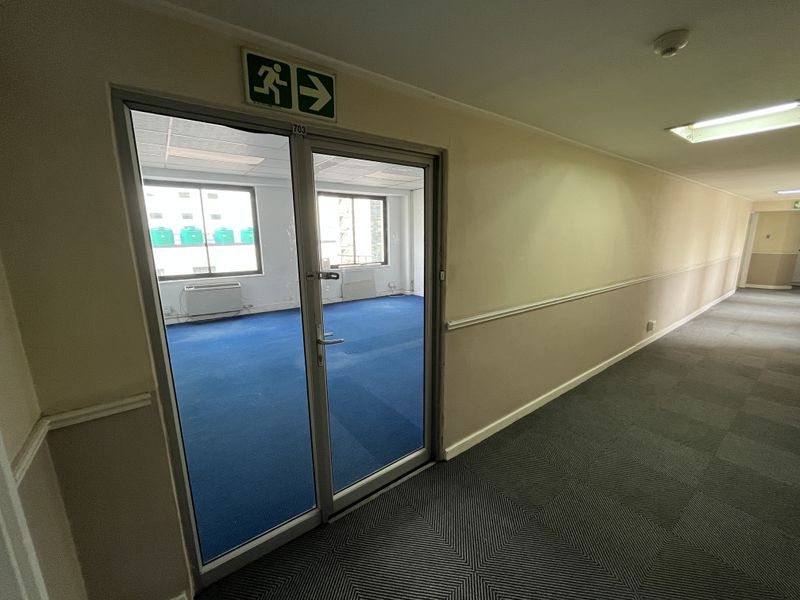 A view of an office hallway with carpeted flooring, chair rail detailing, and a glass-paneled door leading into an office suite.